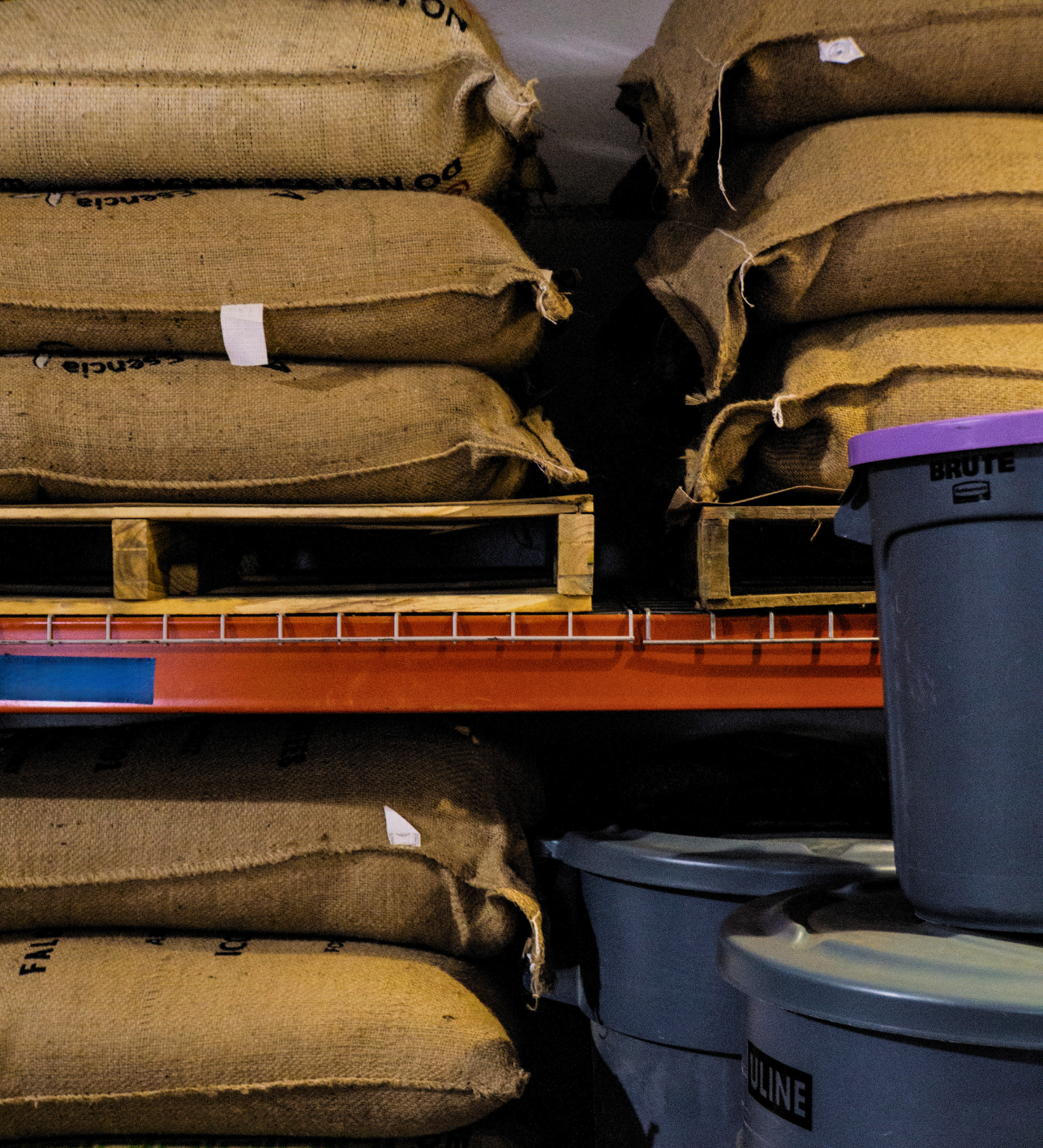 Burlap sacks of green coffee beans stacked on wooden pallets in a warehouse — specialty coffee copacking and retail fulfillment storage.